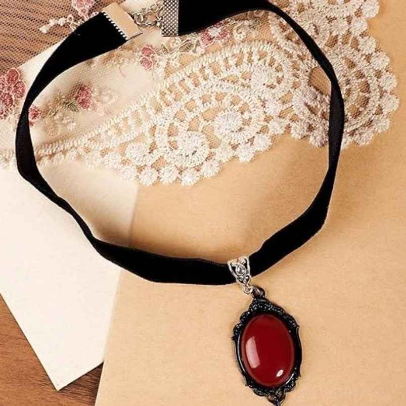 Flat lay of black velvet Gothic choker necklace with red oval gemstone and lobster clasp on lace background