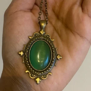 Close-up overhead detail of green Victorian steampunk necklace pendant showing beaded bronze frame and cat-eye emerald stone in hand