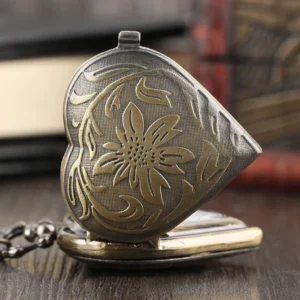 Closed heart-shaped steampunk pocket watch locket with embossed golden floral patterns on dark bronze base, three-quarter side angle view on vintage wooden desk