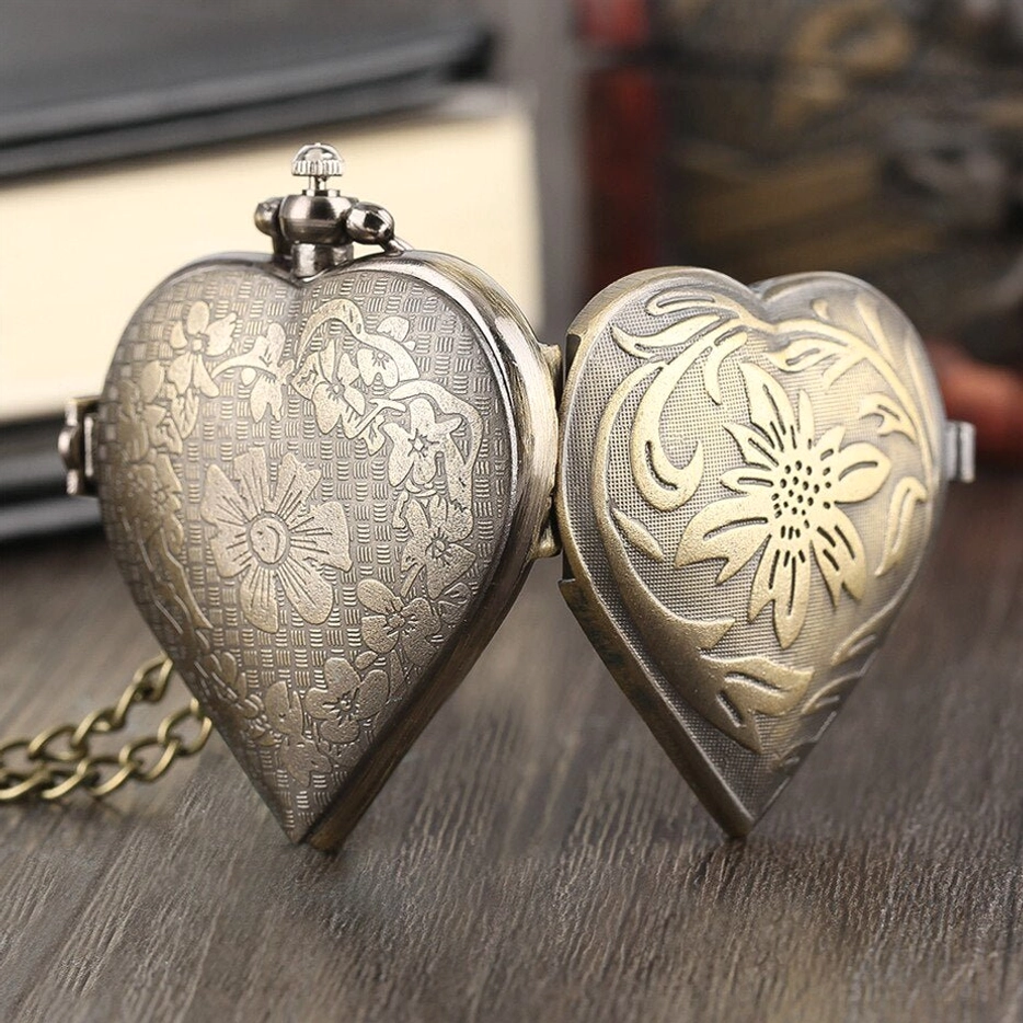 Two matching heart-shaped steampunk pocket watch lockets displaying antiqued bronze finish with engraved floral designs, flat front view on vintage wooden surface