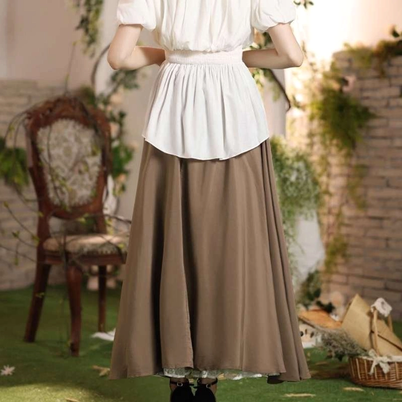 High-waisted vintage steampunk skirt on female model in garden courtyard rear view, paired with cropped ruffled white top, flowing brown fabric detail