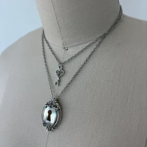 Double-strand lock and key layered necklace featuring ornate oval lock pendant with keyhole detail and silver-toned curb chain on mannequin neck