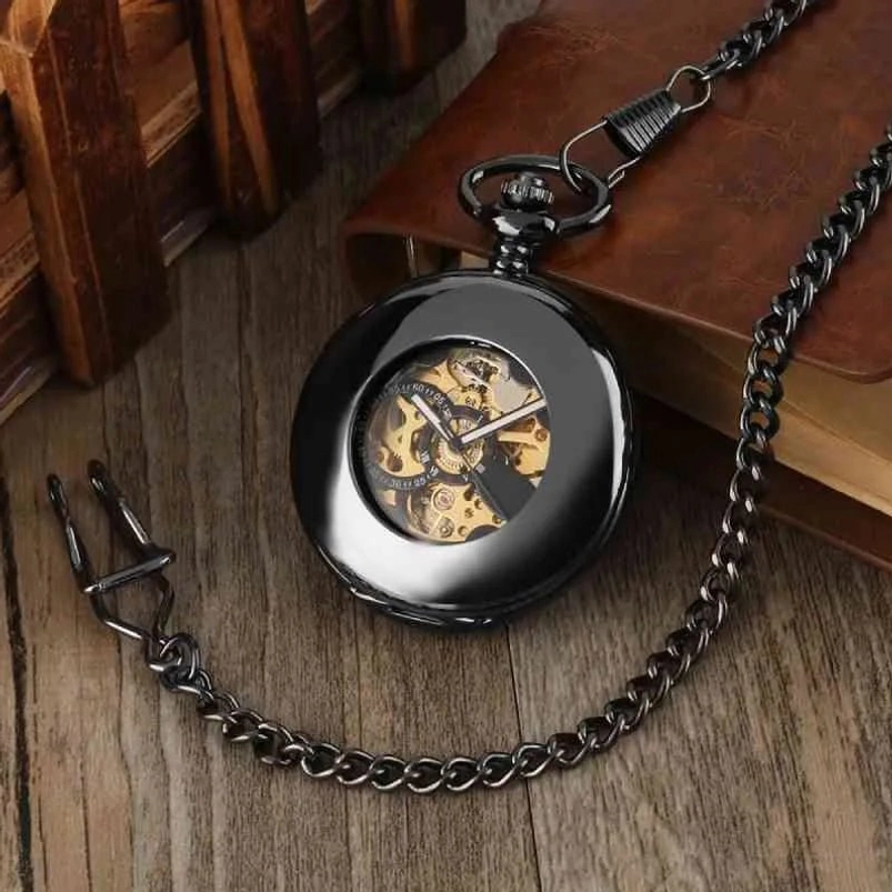 Black steampunk pocket watch with curb chain shown from low angle on leather notebook, glossy metal casing with visible golden gears