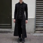 Men's steampunk long coat front view with brass buttons and layered vest overlay, worn by male model on urban street