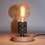 Minimalist steampunk table lamp with natural wood base and knurled aluminum stand featuring warm Edison bulb illuminated in minimal indoor setting