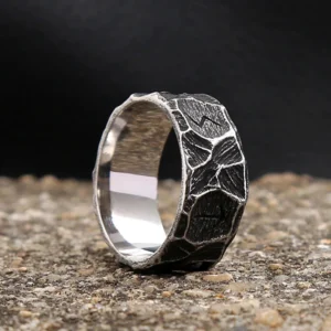 Nordic rune steampunk ring three-quarter view showing oxidized blackened exterior with carved Norse runes and polished inner band on gravel surface