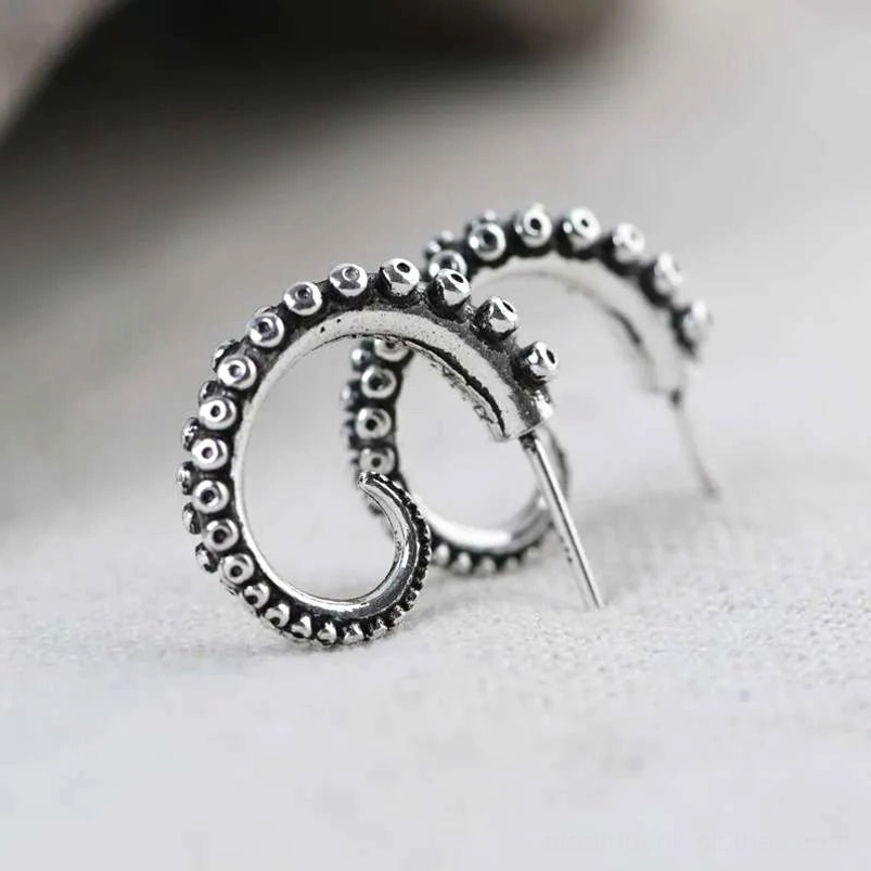 Low three-quarter side view of antiqued silver octopus earrings showing raised suction cup details and pierced stud style on light neutral tabletop