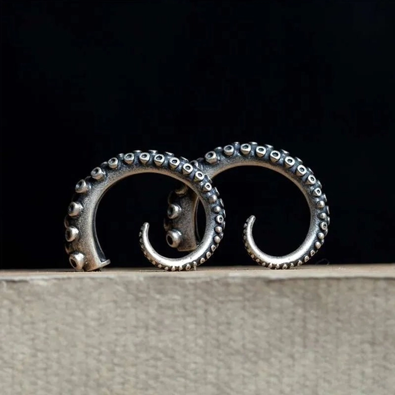 Octopus tentacle steampunk stud earrings with antiqued silver finish and detailed suction cup texture, displayed on dark backdrop with light fabric