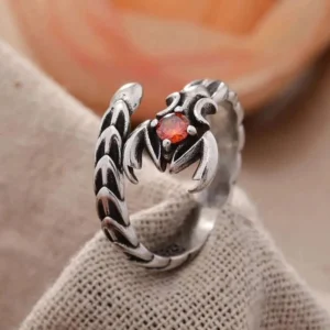 Vintage scorpio steampunk ring with oxidized silver finish and red gemstone, displayed on linen fabric with rose backdrop - top-down oblique view