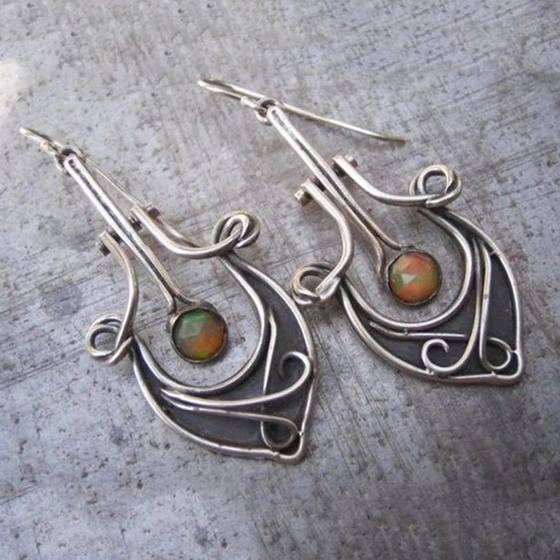 Oxidized silver wire-wrapped steampunk dangle earrings with faceted gemstone inlay and intricate scrollwork hollow pattern, showcasing Victorian-industrial design aesthetic