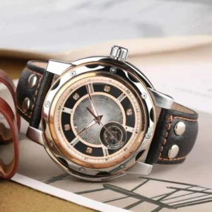 Parisian steampunk automatic watch with two-tone sunburst dial and black leather strap featuring silver rivets, oblique angle view on wooden desk