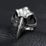 Raven skull steampunk ring front view, aged silver metal with hollow carved bird skull design and realistic beak details on dark leather background