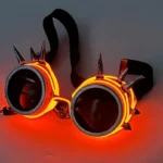 Red LED steampunk goggles with orange glowing EL wire and polished metal spikes, overhead flat lay on dim studio background