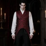 Red Victorian steampunk waistcoat full front view on male model in gothic candlelit chamber, showing double-breasted antique bronze buttons and asymmetric high-low tailcoat hem with paisley jacquard fabric