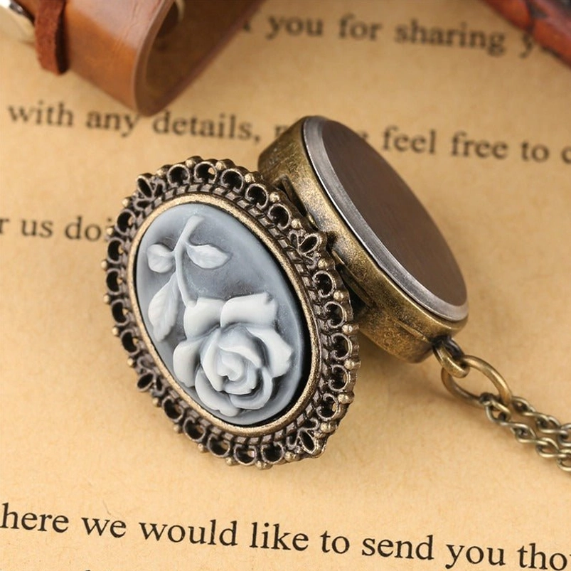 Reversible rose cameo pocket watch necklace on vintage printed paper background, open to show smooth brushed metal back cover and twisted bronze chain design