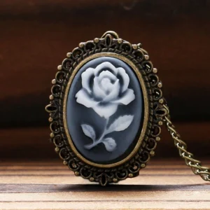 Close-up view of oval rose cameo pendant with filigree bronze frame worn on wooden surface, displaying gray-white rose design and ornate metalwork detail