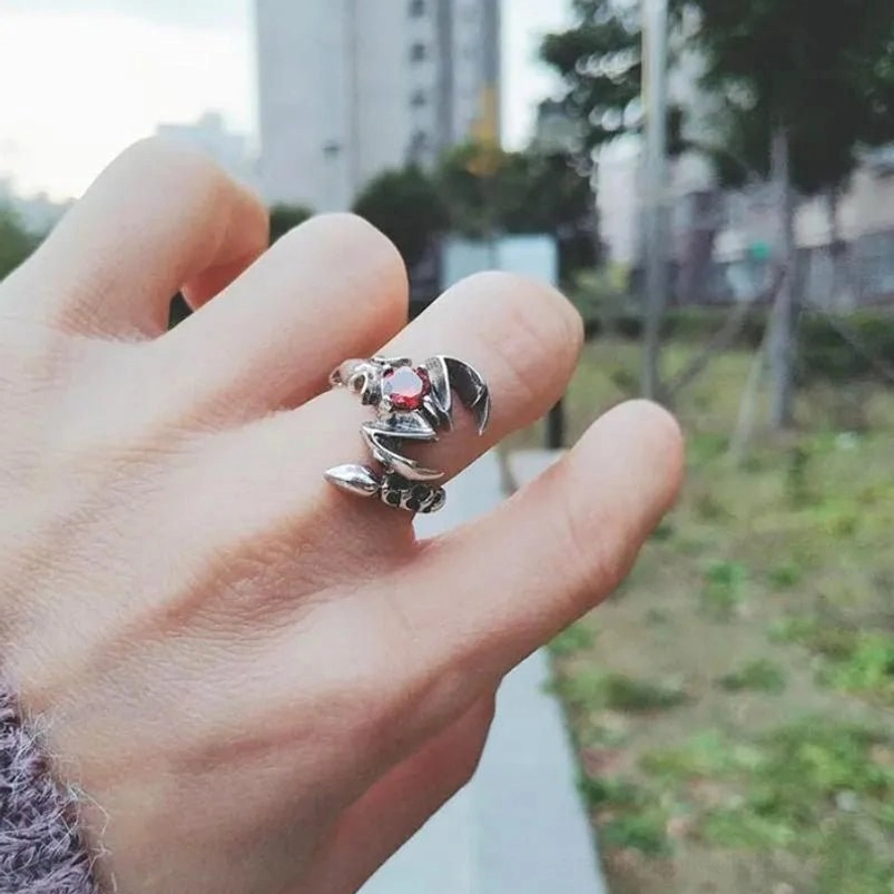 Oxidized scorpio steampunk ring worn on female middle finger with knitted sleeve cuff, outdoor sidewalk setting with greenery