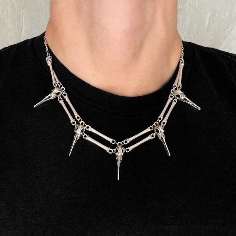 Silver V-shaped bird skull necklace worn on unisex model, displaying gothic punk-inspired layered metal design