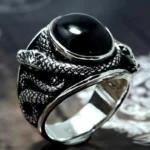 Silver snake steampunk ring with intricate engraved scales and black oval gemstone inlay, photographed from side overhead view showcasing detailed snake head design against dark vintage backdrop