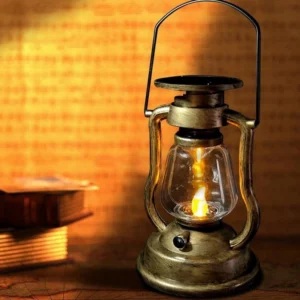 Vintage solar LED steampunk kerosene lantern with brass gold metal frame and clear glass shade on antique desk with books