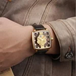 Square steampunk watch with gold case and brown leather band worn on male wrist, showcasing daily casual wear styling with brown jacket