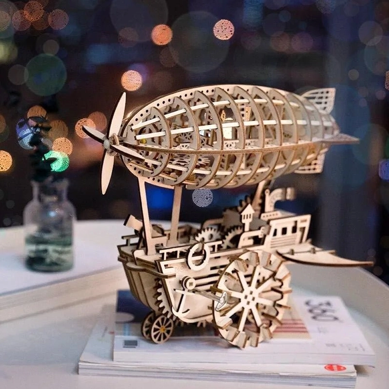 Steampunk airship 3D wooden model front three-quarter view displayed on stacked books with glass jar decoration and nighttime bokeh background