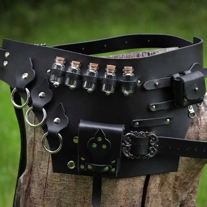 Steampunk alchemist potion waist belt featuring black matte PU leather, five corked glass vials, ornate antique metal buckles, D-rings, and decorative studs - front three-quarter close-up view on wooden stump with grass background