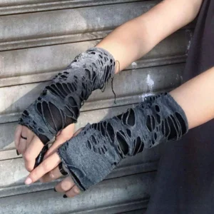 Distressed steampunk fingerless arm sleeves - side eye-level view of two human arms wearing charcoal grey torn knit fabric gloves with exposed frayed hems against outdoor metal shutter background