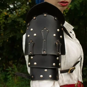 Close-up front detail of steampunk leather shoulder pauldron featuring multi-layered black vegan leather, decorative hand-stitching, and brass metal fasteners with industrial rivet placement