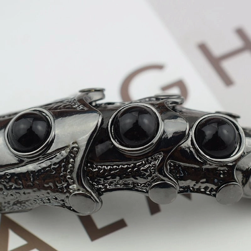 Finger armor ring flat lay composition featuring three round black resin gems aligned, embossed metal architecture, and polished gunblack coating