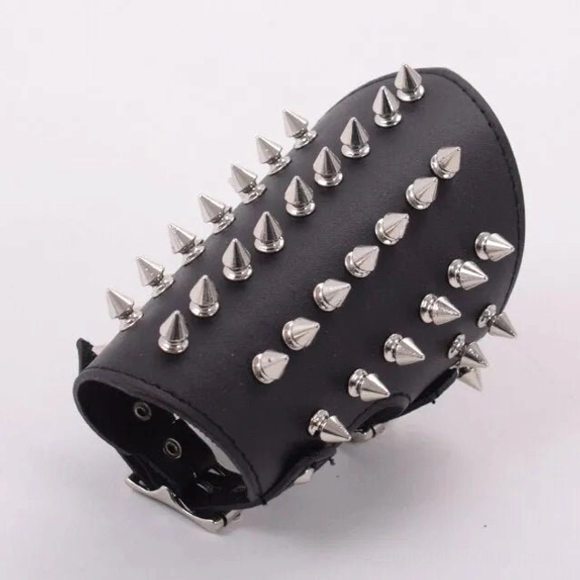 Tall conical spike steampunk wrist guard with long metal spikes and round studs, high angled flat lay studio shot showing three-dimensional texture