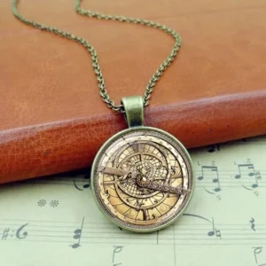 Steampunk astrolabe pendant necklace with bronze tone metal dial and glass cover, displayed on vintage leather and sheet music for authentic industrial aesthetic