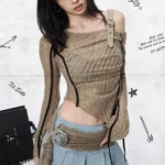 Asymmetrical steampunk off-shoulder ribbed top front three-quarter view with khaki knit fabric, black side trims, leather shoulder strap, and fabric flower waist decoration on female model