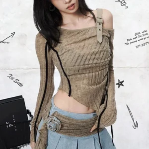 Asymmetrical steampunk off-shoulder ribbed top front three-quarter view with khaki knit fabric, black side trims, leather shoulder strap, and fabric flower waist decoration on female model