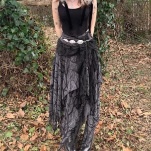 Steampunk asymmetrical midi skirt with bare branch print worn by model in outdoor woodland setting, showcasing layered lace sash and irregular hem