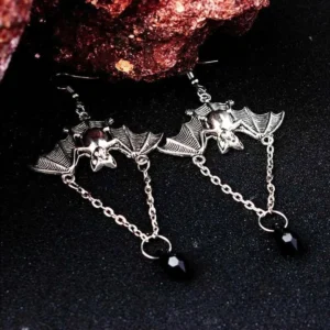 Antique silver bat steampunk drop earrings with black teardrop pendants and chain details, displayed on dark studio background with red mineral decor