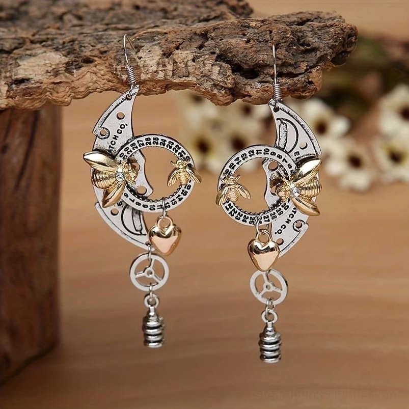 Steampunk bee drop earrings with dual-tone silver and gold metals, featuring intricate gear and heart charms on wooden table with floral background