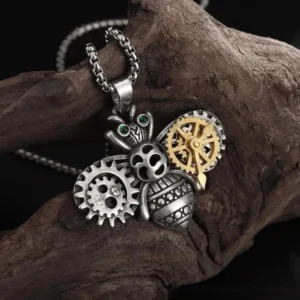 Steampunk bee necklace pendant with brass and silver dual-tone metalwork, green rhinestone eyes, gear decorations, and vintage matte finish displayed on dark wood background - front left angle view