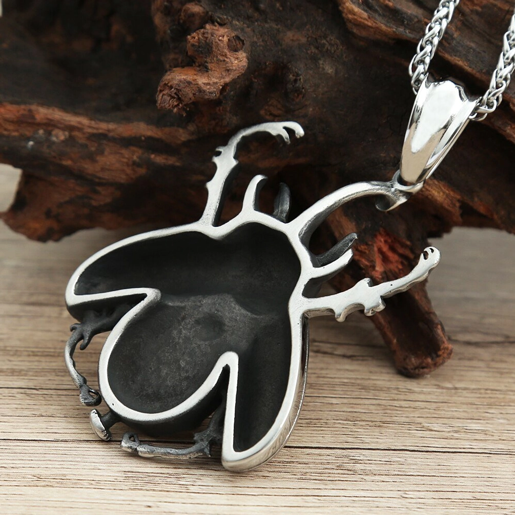 Back view of steampunk beetle pendant showing hollow metal frame, matte black interior, and beetle outline detail on wooden table