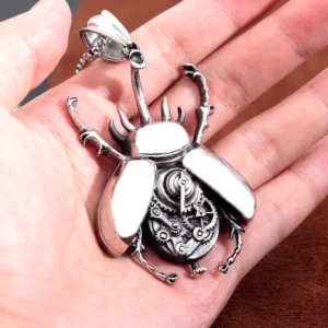 Close-up of steampunk beetle pendant held in palm, showing realistic beetle shape and detailed gear core with vintage silver patina on brown fabric