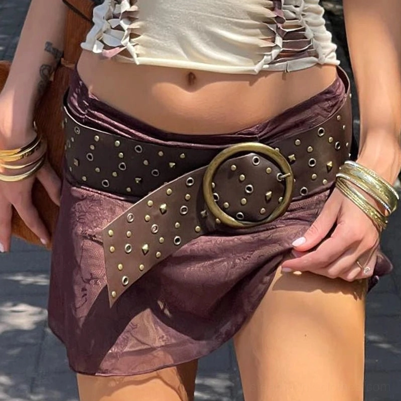 Front close-up waist view of vintage steampunk belt with asymmetrical leather tail, bronze round buckle, model wearing stacked bracelets and outdoor sunny setting