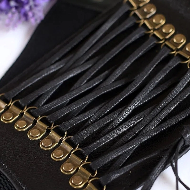 Close-up detail view of steampunk corset waistband showing premium leather laces and antique bronze metal fittings, top-down tabletop photography with purple floral styling accent