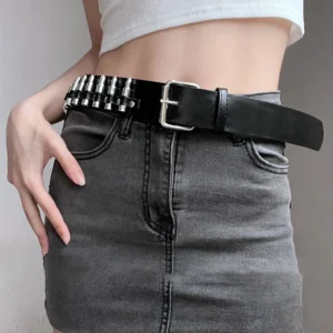 Black bullet studded steampunk gothic belt with square metal pin buckle, styled with white cropped top and dark denim skirt, frontal waist view demonstrating outfit integration