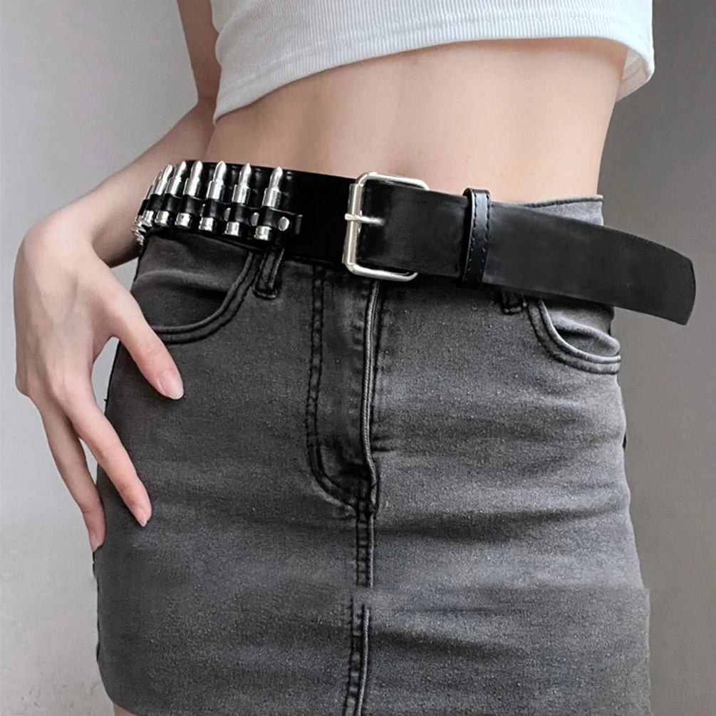Black bullet studded steampunk gothic belt with square metal pin buckle, styled with white cropped top and dark denim skirt, frontal waist view demonstrating outfit integration