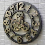 Steampunk wall clock with Big Ben design, vintage bronze-gold finish, 3D Arabic numerals, displayed on gray brick wall, hollow industrial frame design