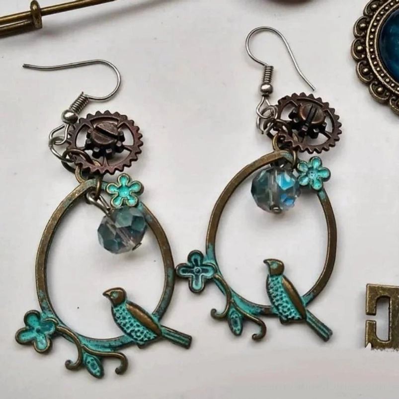Steampunk bird loop earrings with verdigris bronze frame, intricate gears, blue crystal beads, and delicate clover accents displayed in flat lay with spare jewelry components