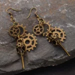 Vintage bronze bird skull gear drop earrings in Steampunk style, displayed on dark slate background with intricate mechanical details and authentic patina finish