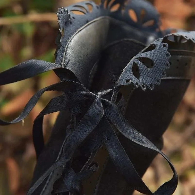 Close-up detail of black steampunk boots showing satin ribbon laces and scalloped leather trim on the lace-up front
