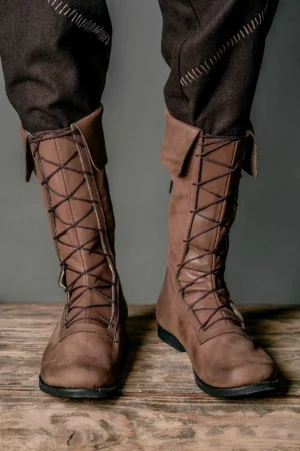 Front view of steampunk boots showing detailed front lacing system, black rubber sole, and premium brown leather finish on male model