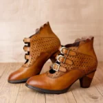 Tan leather steampunk ankle boots featuring triple metal buckle straps, perforated geometric cutout design, and scalloped heel trim shown in front and side profile view